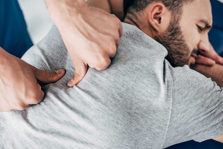 Person applying a wrapped ice pack to the lower back while seated safely at home.
