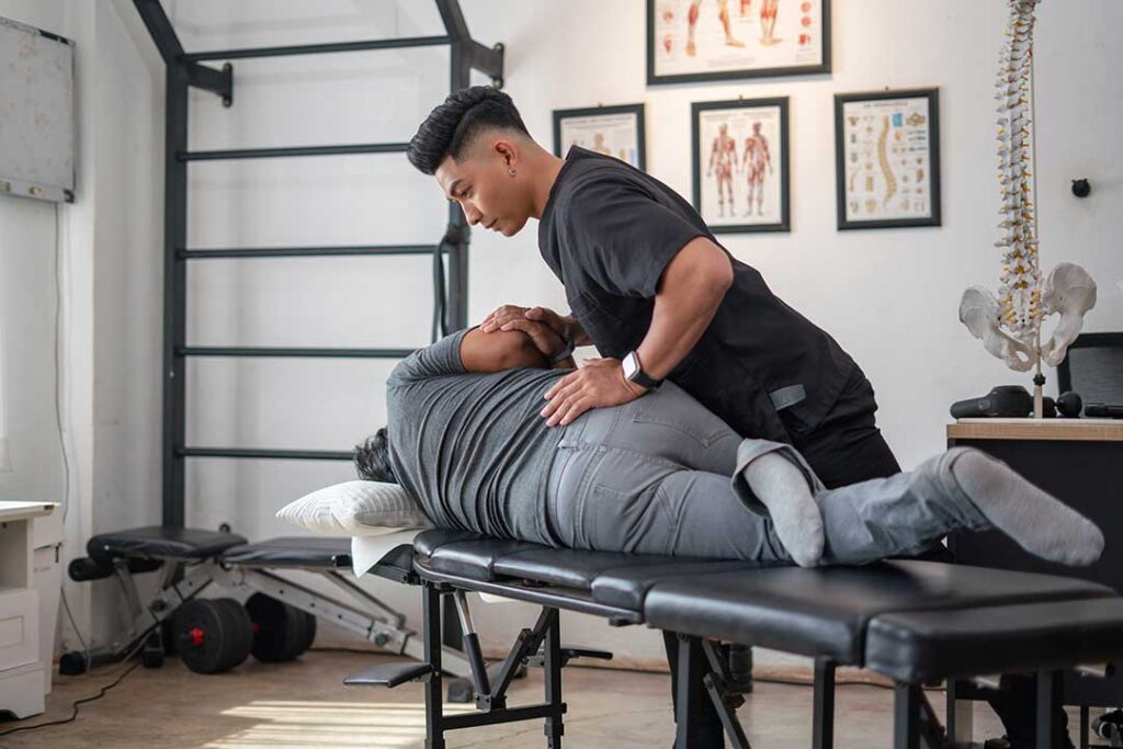 Clinician assessing a seated adult’s spinal movement in a bright examination room