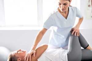 Older adult performing a gentle mobility exercise beside a sturdy chair with a caregiver nearby.